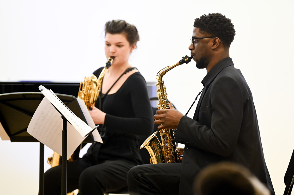 Two students playing the saxophone in smart black attire.